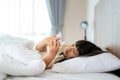 Happy Asian girl looking at mobile phone while lying on the bed in bedroom at home in morning after wake up preparing go to school Royalty Free Stock Photo