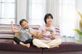 Happy Asian girl with sister playing video game using joystick or controller while sitting on sofa Royalty Free Stock Photo