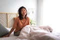 Happy asian girl sitting on bed waking up in the morning in cozy bedroom at home looking at camera. Copy space. Royalty Free Stock Photo