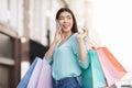 Happy Asian Girl Walking With Lots Shopping Bags And Talking On Cellphone