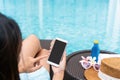 Happy Asian girl wearing swimsuit lying on sunbed and using smart phone relaxing at the poolside with hat, towel, smartphone and Royalty Free Stock Photo