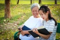 Happy asian granddaughter reading a book and senior grandmother together at summer park,loving child girl holding book sitting on Royalty Free Stock Photo