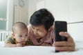 Happy Asian Grandmother and little baby boy or Grandchild playing and taking selfie photos with smartphone together Royalty Free Stock Photo