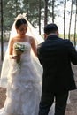 Happy Asian groom help his bride dress up in a pine forest background