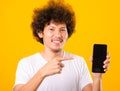 Happy asian handsome young man with curly hair holding blank screen smart phone and pointing finger Royalty Free Stock Photo