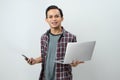 Happy asian indonesian man holding smartphone and laptop computer on isolated background Royalty Free Stock Photo