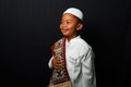 Happy Asian kid wearing koko and a cap bring prayer rug isolated on black background Royalty Free Stock Photo