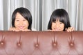 Happy asian kids peeking a sofa