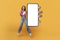 Happy asian lady demontrating empty smartphone screen while jumping up on yellow studio background, mockup Royalty Free Stock Photo