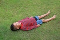 Happy Asian little boy lying down on green lawn. Kid lies on grass looking on sky Royalty Free Stock Photo