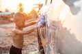 Happy asian little boy playing white soap and using blue sponge to washing the car at outdoor in sunset time Royalty Free Stock Photo