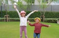 Happy Asian little boy and young girl child wearing straw hat standing and waving goodbye with looking camera in the garden Royalty Free Stock Photo