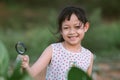 Happy asian little child girl looking through a magnifying glass on green leaf tree in the park Royalty Free Stock Photo