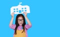 Happy asian little child girl in pink-yellow dungarees holding mock-up paper school looking straight at camera isolated on blue Royalty Free Stock Photo