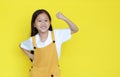 Happy asian little child girl showing his muscle with looking camera isolated on yellow background with copy space. Strong kid in