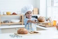 Happy Asian little cute kid girl wear chef hat and apron holding showing homemade whole grains bread on wooden tray in kitchen Royalty Free Stock Photo