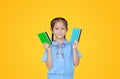 Happy Asian little girl in school uniform holding account book isolated on yellow background. Schoolgirl with bank passbook. Money Royalty Free Stock Photo