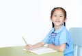 Happy Asian little girl in school uniform writing on notebook at desk isolated on white background. Schoolgirl and Education Royalty Free Stock Photo
