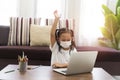 Happy Asian little girl using laptop computer with wearing medical mask, Student learning virtual internet online Royalty Free Stock Photo