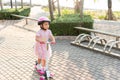 Happy Asian little kid girl wear safe helmet playing pink kick board on road in park outdoors on summer day Royalty Free Stock Photo