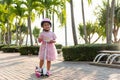 Happy Asian little kid girl wear safe helmet playing pink kick board on road in park outdoors on summer day Royalty Free Stock Photo