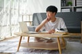 A happy Asian male college student using his laptop at a coffee table in his living room Royalty Free Stock Photo