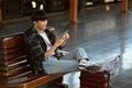 Happy Asian male traveler with suitcase using mobile phone while waiting train. Travel and vacations concept. Royalty Free Stock Photo