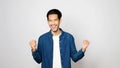 Happy asian man arm up with successful achievement looking at camera while standing over isolated gray background