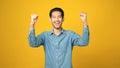 Happy asian man arm up with successful achievement while standing over isolated yellow background