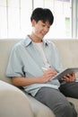 Happy Asian man in casual clothes relaxing on sofa in his living room and using his digital tablet Royalty Free Stock Photo