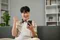 A happy Asian man celebrating his good news while sitting on a sofa in the living room Royalty Free Stock Photo