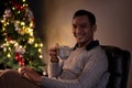 A happy Asian man is enjoying his coffee while relaxing in his living room on a Christmas night Royalty Free Stock Photo