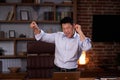 Happy Asian man enjoying music using a laptop and dancing in modern workroom. Man freelancer having fun after work Royalty Free Stock Photo