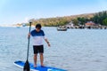 Happy Asian man with eyeglasses in casual clothes standing on stands up paddleboard