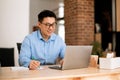 Happy asian man looking at laptop screen and writing in notebook, sitting at workplace at home office, selective focus Royalty Free Stock Photo