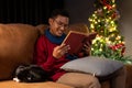 A happy Asian man is reading a book on a couch while his cat is sleeping beside him Royalty Free Stock Photo