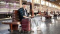 A happy Asian man sitting on a bench at a railway station with his bags, waiting for his train Royalty Free Stock Photo