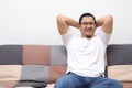 Happy Asian man sitting and thinking on his sofa at home in the living room, cheerful smiling expression Royalty Free Stock Photo