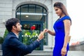 Happy asian man in stylish black suit falling knee in front of his beautiful woman in blue long dress asking proposal Royalty Free Stock Photo