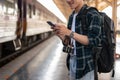 A happy Asian man tourist using his smartphone while standing at a platform in a railway station Royalty Free Stock Photo