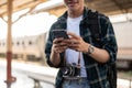 A happy Asian man tourist using his smartphone while standing at a platform in a railway station Royalty Free Stock Photo