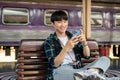 A happy Asian man is using his phone while waiting for his train at a railway station Royalty Free Stock Photo
