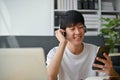 A happy Asian man wearing headphones, choosing music playlists on his phone Royalty Free Stock Photo