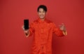 Happy Asian man wearing traditional dress showing mobile phone blank screen isolated on red background Royalty Free Stock Photo