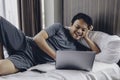 Happy Asian man is working with his laptop on his bed. Concept of freelancer successful lifestyle Royalty Free Stock Photo