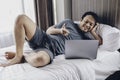 Happy Asian man is working with his laptop on his bed. Concept of freelancer successful lifestyle Royalty Free Stock Photo