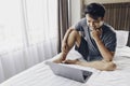 Happy Asian man is working with his laptop on his bed. Concept of freelancer successful lifestyle Royalty Free Stock Photo