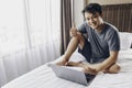 Happy Asian man is working with his laptop on his bed. Concept of freelancer successful lifestyle Royalty Free Stock Photo