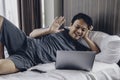 Happy Asian man is working with his laptop with video call in a bed. Concept of freelancer successful lifestyle Royalty Free Stock Photo
