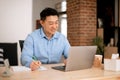Happy asian middle aged man freelancer using laptop and taking notes while working at home, sitting at desk, copy space Royalty Free Stock Photo